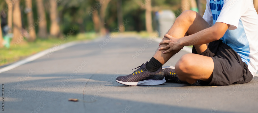 Runner sitting on the road holding an injured ankle